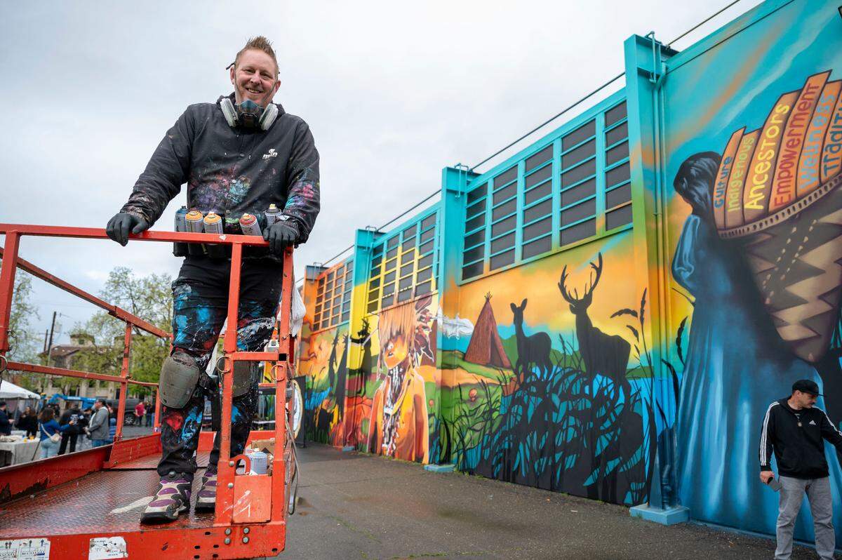 Artist Shane Grammer stands on a lift Saturday after adding some final touches to a mural that celebrates the historic name change of Sutter Middle School to Miwok Middle School. His nonprofit organization, Hope Through Art, partnered with youth artists in the Native Dads Network’s youth leadership development program and the Sacramento City Unified School District to create the mural at the school.