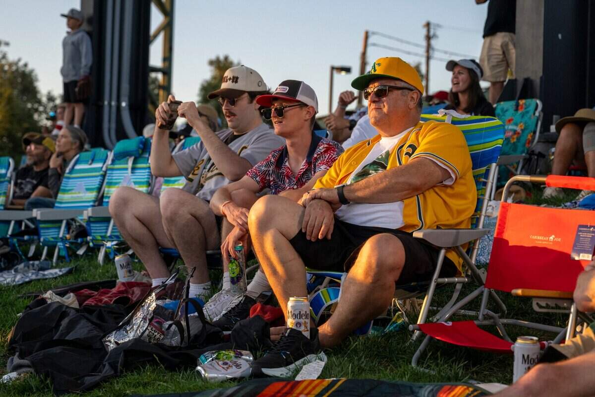 Ed Hickenbottom, right, sits on the center field lawn during a baseball game between the San Francisco Giants and the Athletics at Sutter Health Park on July 4.