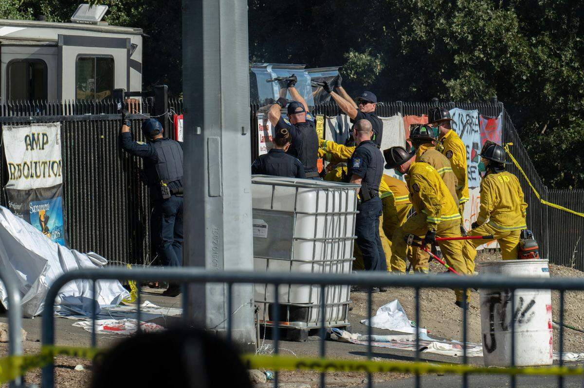 Sacramento police and firefighters work to break down the Camp Resolution fence, which residents had welded shut and fortified with barbed wire, before removing the homeless encampment on Monday.