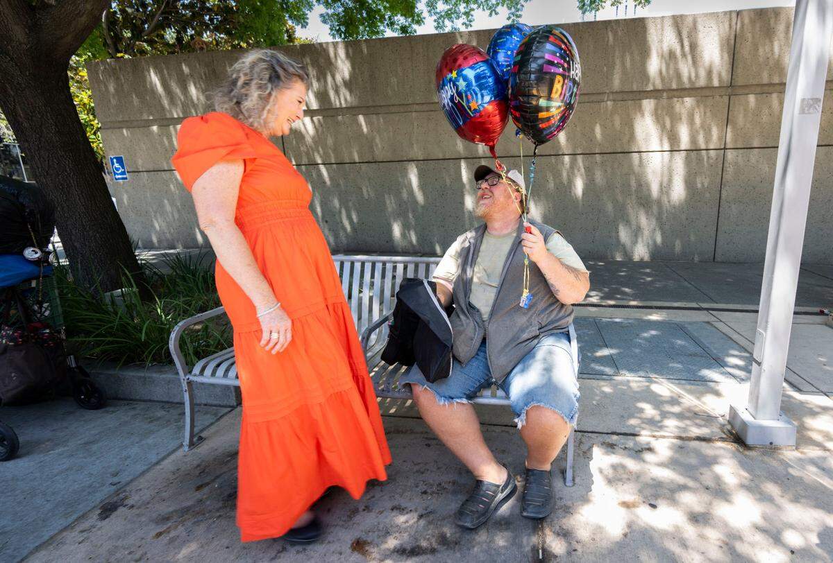 Maria Montano, a social worker at the Sacramento Public Library, visits last month with Paul Jackson as he sits on a bench near the library where he used to sleep. Montano gave Jackson some balloons and presents the day after his birthday.