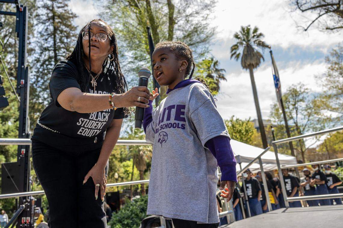 Ramona Bishop, president of Elite Public Schools, holds a microphone for Raine Oler, 4, as she recites a poem “Hey Black Child” by Useni Eugene Perkins on Tuesday, April 11, 2023 at a Black in School Coalition rally and march at Capitol Park in Sacramento in opposition to Gov. Gavin Newsom’s education budget proposal, which they said doesn’t provide enough funding to narrow the academic achievement gap for Black students.