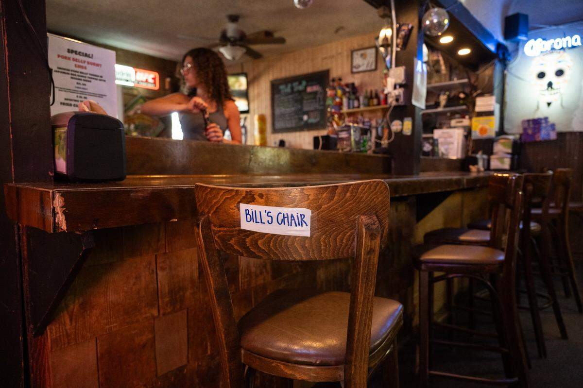 A bar stool labeled “Bill’s Chair” sits empty as Mariah Lukenbill tends the bar at The Trap in Sacramento on Monday.