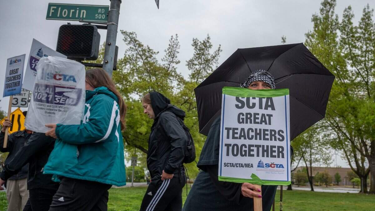 La maestra de Kennedy High School Patricia Juárez lleva un cartel y un paraguas mientras se une a los maestros y personal de apoyo en huelga de Sacramento City Unified, el lunes 28 de marzo de 2022, cerca de su escuela.