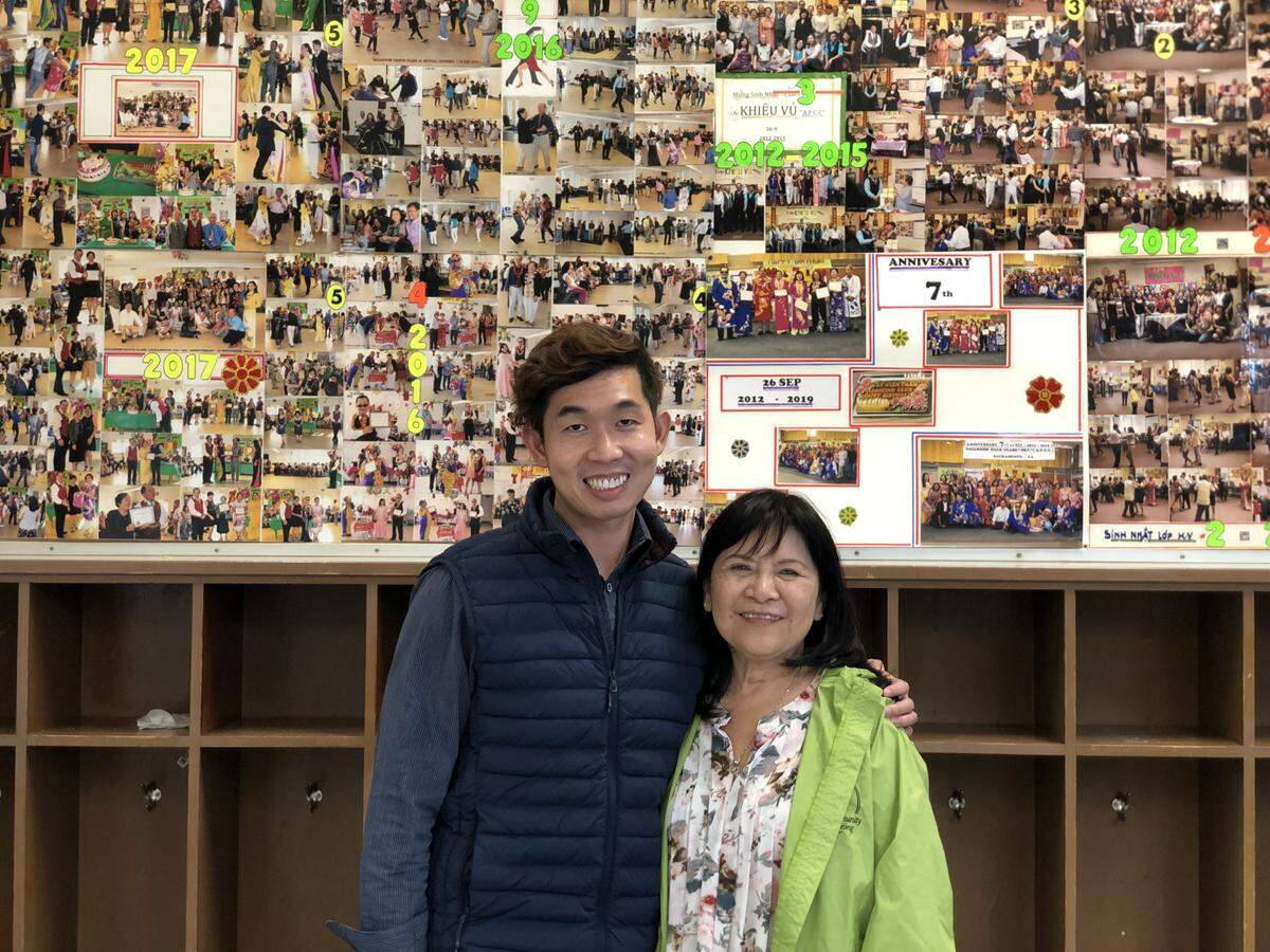 APCC Program coordinators Kent Lou and Vi Pham stand in front of the photos documenting the journey of their class participants since 2012.