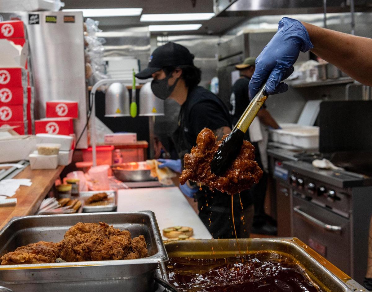Matt Rocha, right, lifts a chicken thigh out of hot oil while Gavin Okamoto, back, makes sandwiches at Nash and Proper’s takeout restaurant on K Street in 2020.