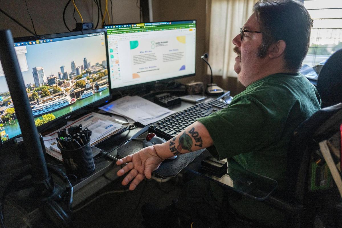 Russell Rawlings usa un micrófono para introducir texto mientras trabaja con su  computadora el martes. Rawlings, un activista de los derechos de los discapacitados que padece parálisis cerebral y depende de los cuidadores de los Servicios de Apoyo a Domicilio de California, trabaja a tiempo completo, pero dice que no podría permitirse un alquiler en Sacramento sin un compañero de casa.