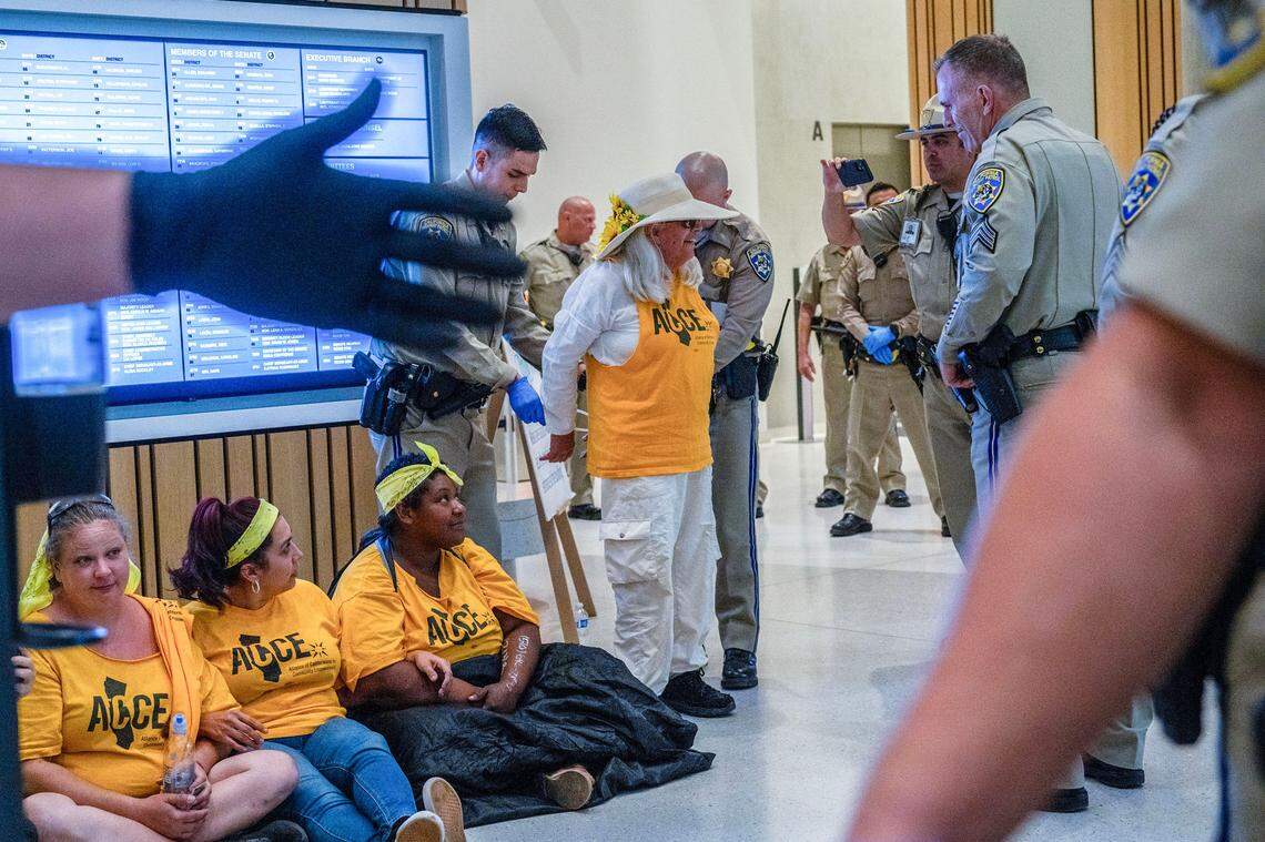 California Highway Patrol officers fasten a zip tie on Elsa Stevens, 71, in the Capitol Swing Space on Thursday while other officers usher protesters from the lobby. Six people, some homeless, were eventually arrested during a sit-in demonstration calling for an end to homeless sweeps and calling on the governor, whose office is in the building, to help build more affordable housing.
