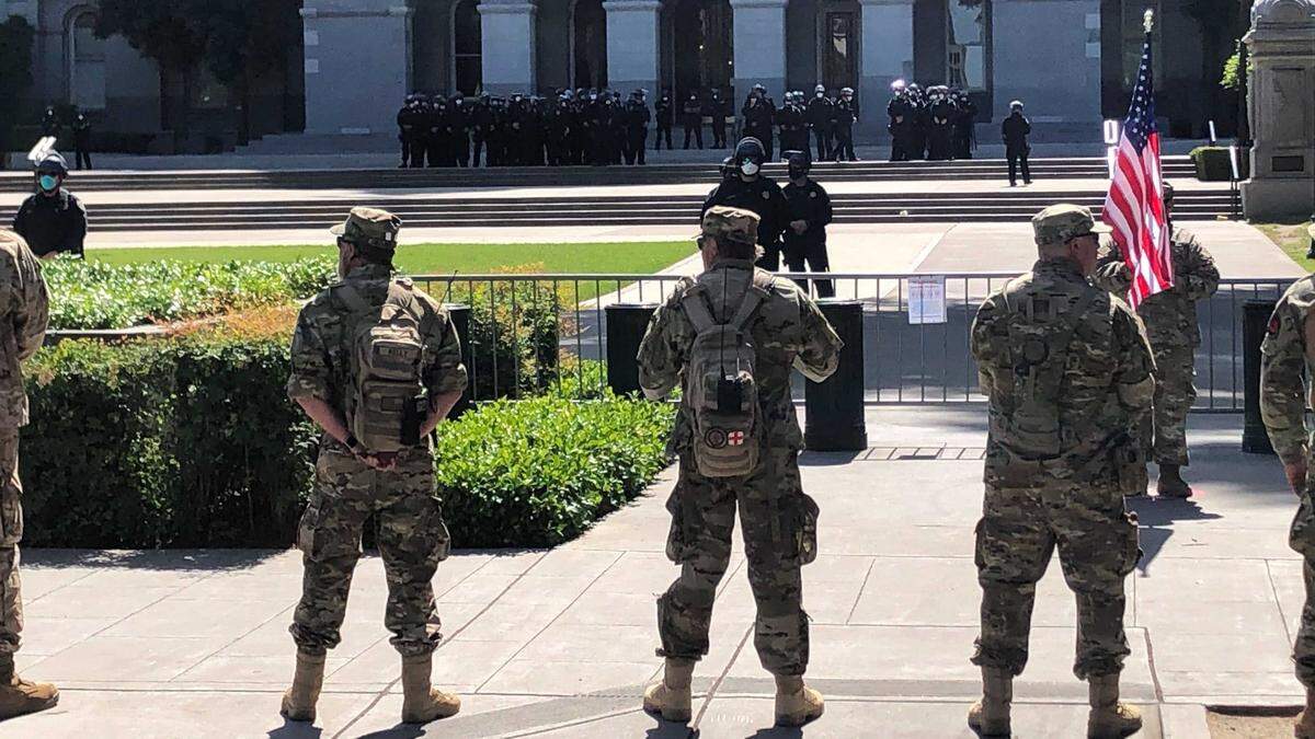 Members of the self-described California State Militia, 2nd regimen, stand at attention along 10th Street on Saturday, May 9, 2020, at the state Capitol in Sacramento, Calif.