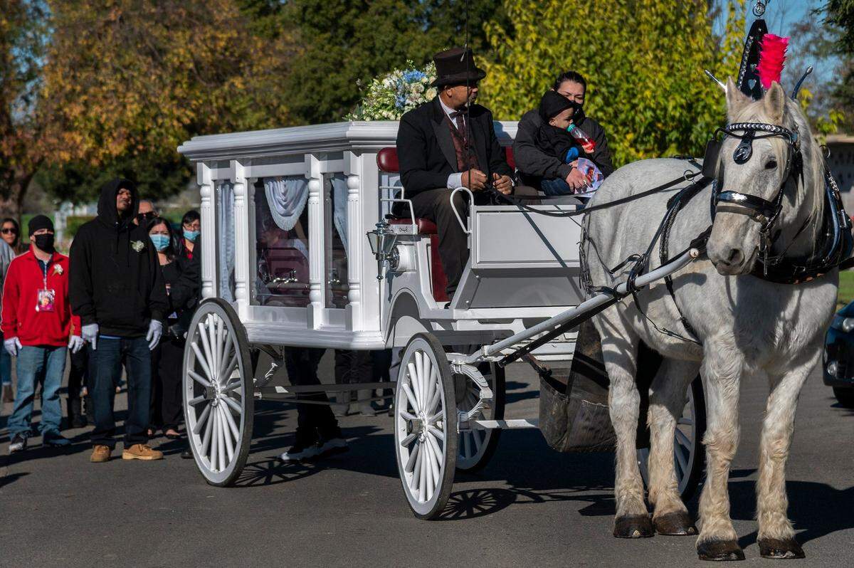 Monica Delgadillo and her infant son Brandon ride in the front of a carriage carrying the casket for her daughter Isabel Delgadillo Martin, who died five days before her eighth birthday, as her father Brandon Martin gets ready to follow the procession to the grave site at Sunset Lawn Chapel of the Chimes cemetery in Sacramento on Dec. 10.
