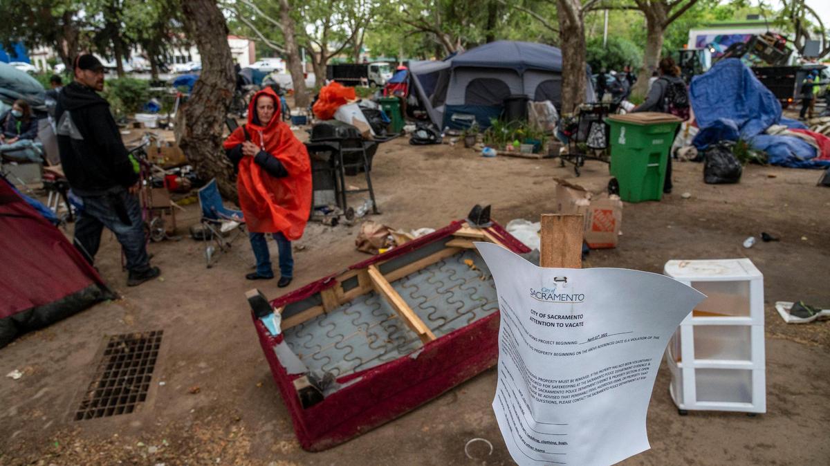 A Sacramento City sign warning the homeless at a Fair Oaks and Howe encampment they need to vacate is in the foreground as residents scramble to move during a homeless sweep in Sacramento on Monday, April 11, 2022.