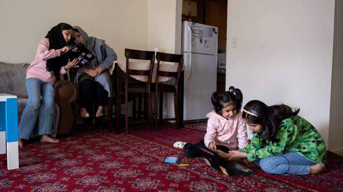 Zakia Ahmadi, 13, shows a school lesson on her computer to mother Marzia Ahmadi, as sisters Zohra, 12, and Bahara, 7, look at a lesson on a laptop in their sparsely furnished Yuba City apartment on Jan. 24, 2025. The family arrived in the United States from Afghanistan in April 2024 after their father Abdul Basir Ahmadi received a special immigrant visa designated for Afghans who worked directly with the U.S. military or its contractors.