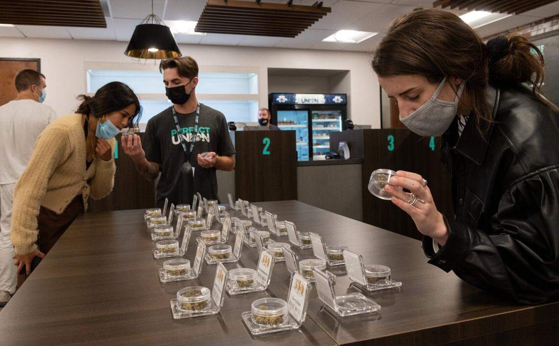 Budtender Dustin DeCarlo holds a sample marijuana bud for a client as another client looks at the variety of buds available for sale at the Perfect Union on Friday, Oct. 22, 2021, in Sacramento.