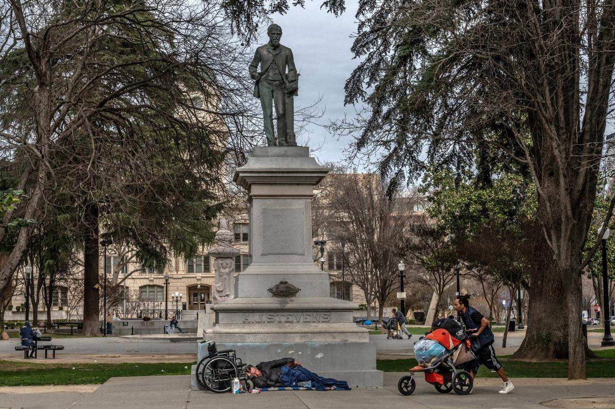 A homeless man sleeps while others push carts near the A.J. Stevens statue in Cesar Chavez Plaza in downtown Sacramento on Feb. 18. It’s not uncommon to see large groups of people sleeping in the park.