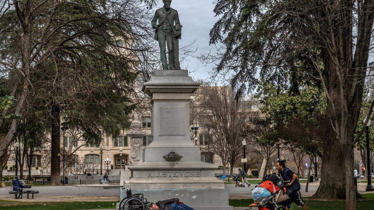 A homeless man sleeps while others push carts near the A.J. Stevens statue in Cesar Chavez Plaza in downtown Sacramento on Thursday, Feb. 18, 2021. It’s not uncommon to see large groups of people sleeping in the park.