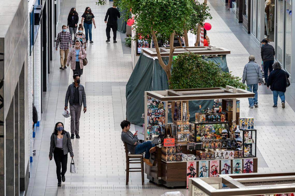 Shoppers at Arden Fair mall in Sacramento wear masks as they pass a seated unmasked worker at an indoor kiosk on Tuesday. California’s indoor mask mandate ends Wednesday, but teachers and students must keep masking up according to state guidelines.