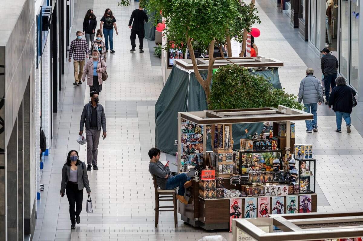 Compradores del centro comercial Arden Fair de Sacramento llevan mascarillas mientras pasan por delante de un trabajador sin mascarilla sentado en un quiosco interior el martes. El mandato de California de uso de mascarillas en interiores finaliza el miércoles, pero los profesores y estudiantes deben seguir usándolas según los lineamientos estatales.