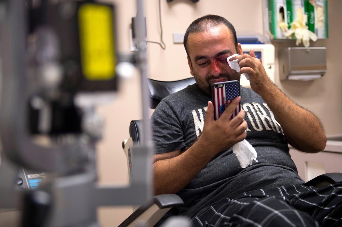 Using his American flag-covered mobile phone as a mirror, Afghan refugee Faisal Razmal wipes excess fluid from his injured eye in 2015 after he was shot in the eye with a flare gun while trying to stop a robbery.