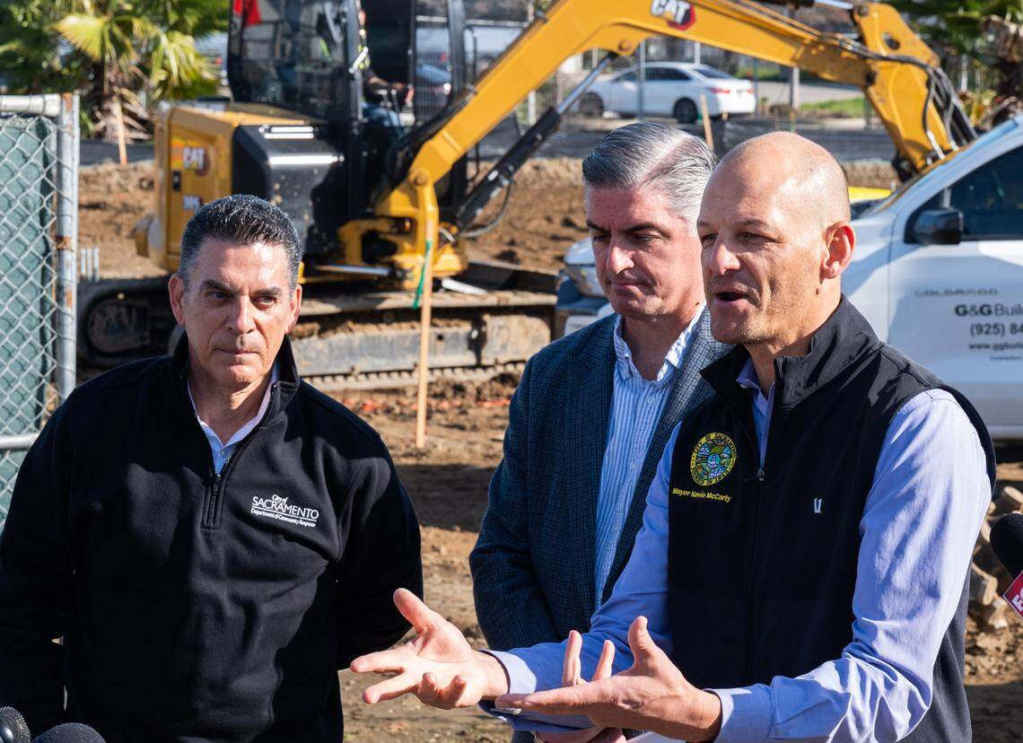 Sacramento Mayor Kevin McCarty, right, speaks as workers build a new safe camping site in the River District on Friday. Department of Community Response Director Brian Pedro, left, and Council Member Phil Pluckebaum, center, joined him at the event. 