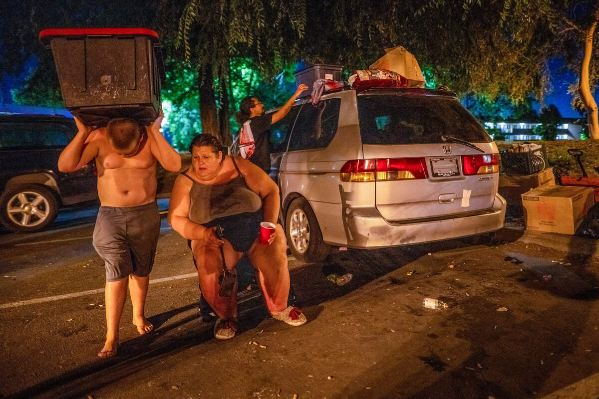 Keith-Dalton Smith, 11, carries his family's belongings past his mother, Amy Heckart, 46, who is disabled, on Wednesday in Sacramento. The family was removing items they had stored on top of their van so it could be towed to another lot within sight of the Motel 6, where they had lived for the past 2-1/2 years.