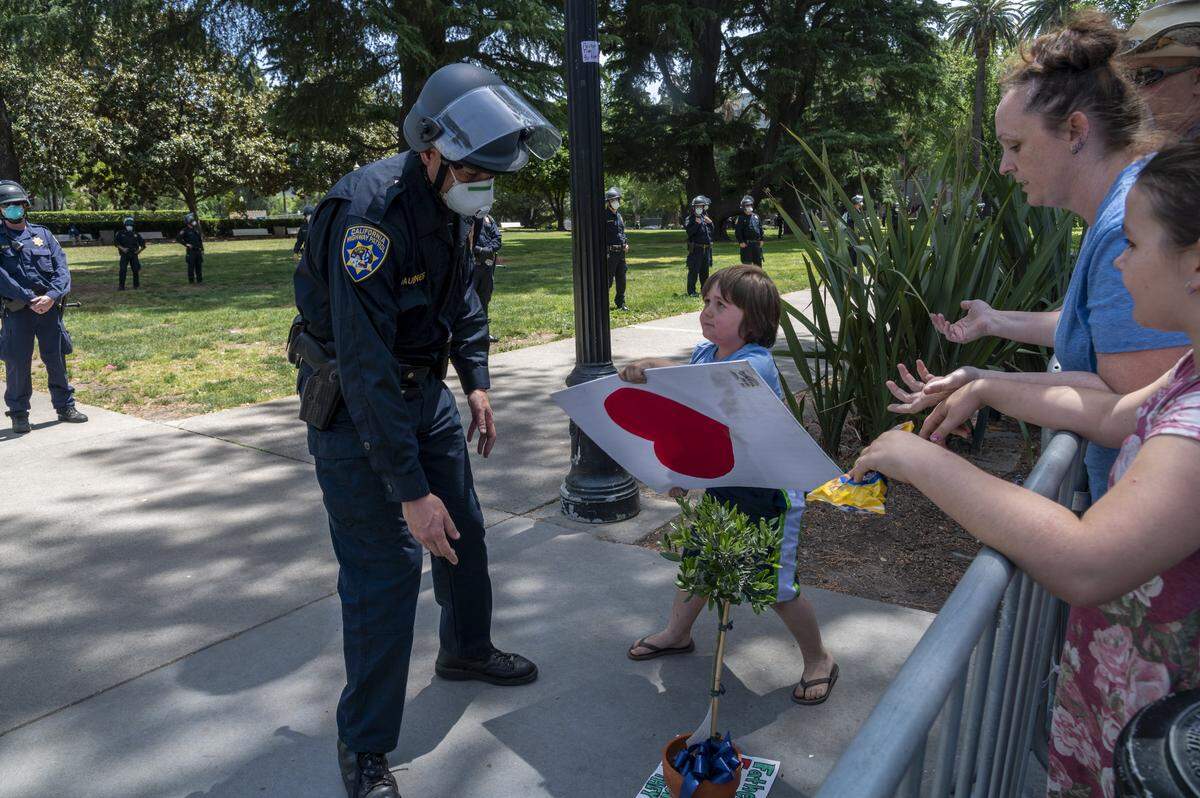 Konner Hoff, 7, tries to give a heart sign to a CHP officer after sneaking under the barrier at a protest at the state Capitol on Thursday, May 7, 2020 in Sacramento. The officer didn’t take it, or the olive tree which he attempt to return to the protesters. The demonstrators were rallying against Gov. Gavin Newsom’s coronavirus stay-at-home order.