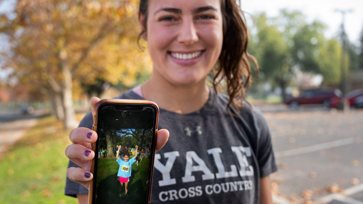 Sophia Karperos holds up her cell phone to show a photo of herself as a second grader when she signed up for the “Runnin’ for Rhett” youth fitness program. She said it sparked a passion for running and now, at 20, she runs varsity cross country track at Yale University.