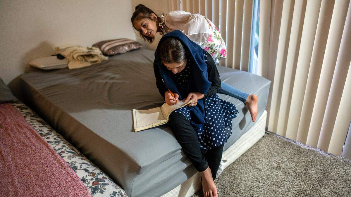 Afghan refugee Zalaikha, 13, practices writing her name in English as her sister Hasiba, 8, peeks over her shoulder on Sept. 20 in Sacramento.
