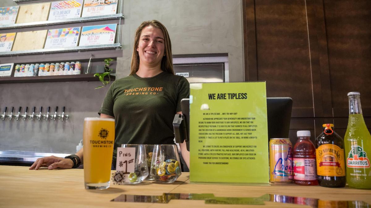 Kristen Madigan, pub manager at Touchstone Brewing Company, stands behind the bar Friday, Aug. 18, 2023, in Sacramento. A sign next to the payment area explains why their establishment is “tipless.”
