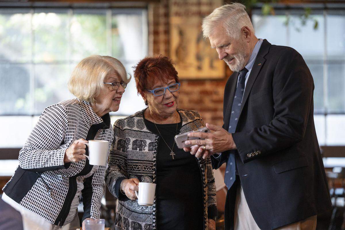 Former Democratic state legislator Dede Alpert, left, and former Republican state legislator Andrea Seastrand, center, look at a photo on the phone of Tom Umberg, who serves as a current state Senator, during a reunion for the California Assembly class of 1990 at Fox & Goose in Sacramento on Wednesday.