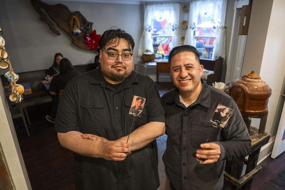 Coatzin Aguilar, left, and Oscar Escobar of Abela’s Midtown hold photos of their grandmothers on Friday. The photos are on cards that are used to manage tables.
