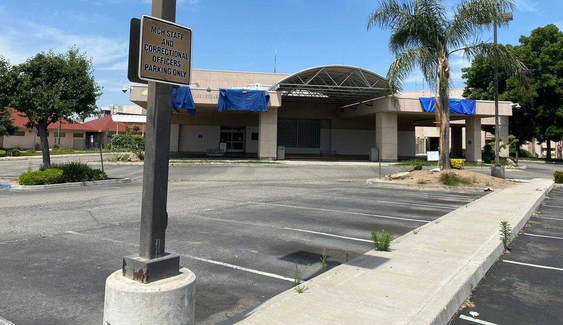An empty parking lot with cracked pavement, faded stripes and weeds popping up are evident at the closed Madera Community Hospital, with blue tarps covering where the facility’s name was formerly displayed, on Tuesday, May 16, 2023. The hospital closed in January.