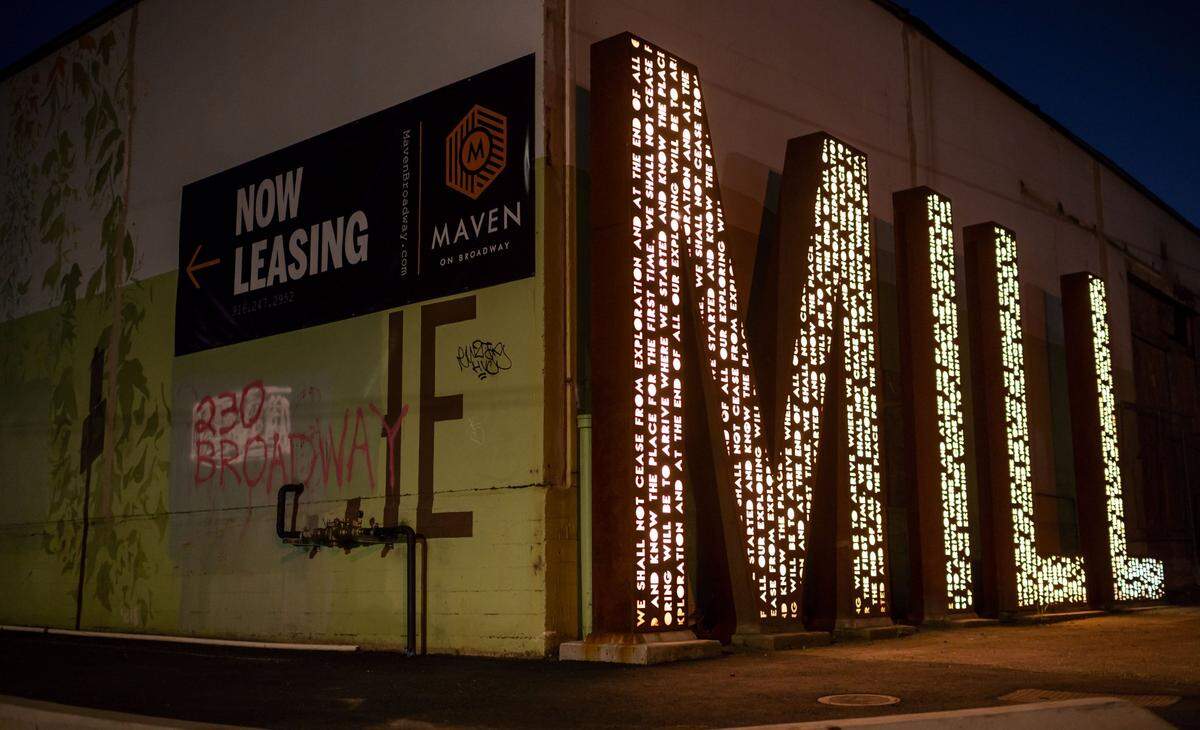 A sign for The Mill development stands in front of an industrial building at Third Street and Broadway.
