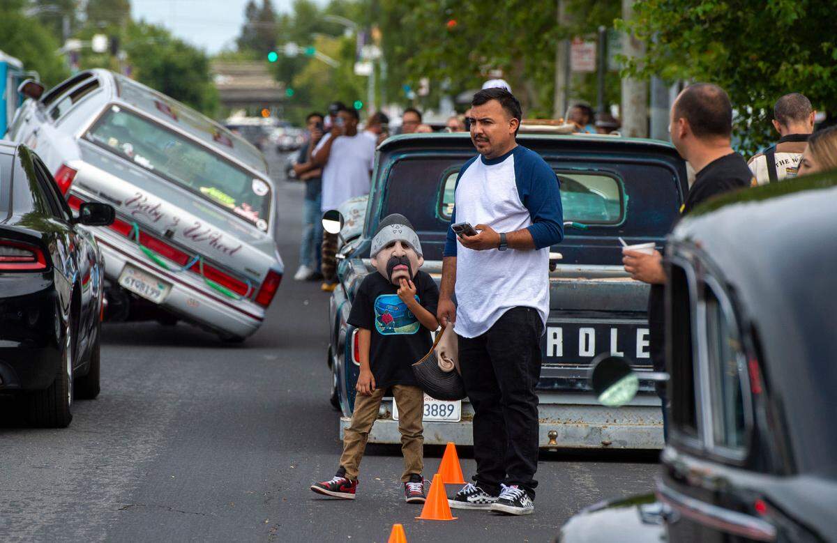 Pablo Martintez Jr, 7, wears a “Homies” mask while standing with his dad, Pablo Martinez as they watch lowriders cruise down Broadway on Saturday. The event turned into a celebration after the city repealed a 34-year anti-cruising ordinance now viewed as discriminatory.