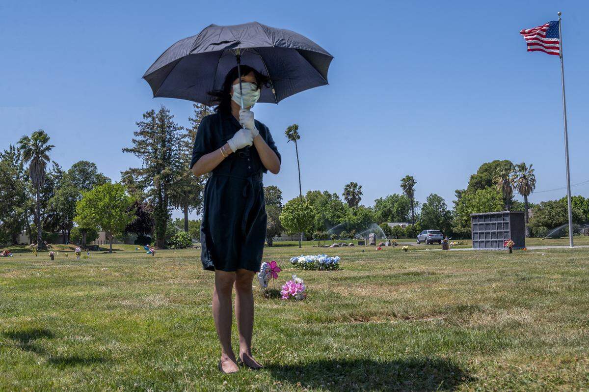 Tracy Nguyen, uses an umbrella to shield the sun while standing alone during the funeral for her boyfriend Dung Tan Nguyen at Sacramento Memorial Lawn on Wednesday, May 6, 2020, during the coronavirus outbreak.