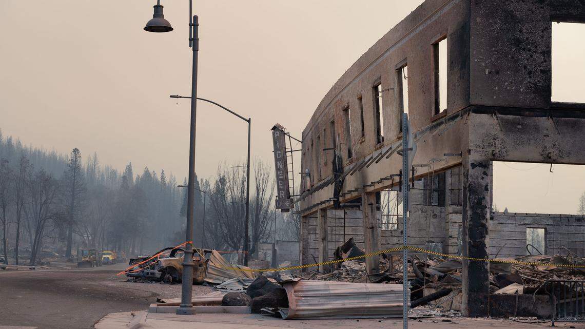 The sign for Pioneer Cafe hangs on the burned and buckling exterior of the Sierra Lodge on Main Street in Greenville on Thursday, Aug. 5, 2021, after the Dixie Fire burned the town. The facade collapsed minutes later, covering the burned car at left in debris.