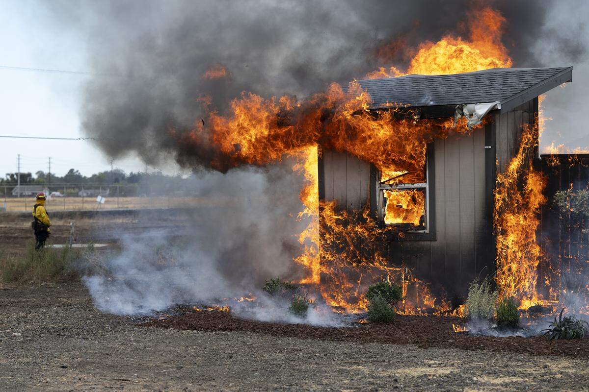 Firefighters watch a temporary structure burn during a burn demonstration at the Sacramento City Fire Training Facility at McClellan Airfield on Wednesday, Sept. 24, 2025. Cal Fire and IBHS hosted the burn to demonstrate the impact of proposed “zone zero” regulations in a wild fire scenario.