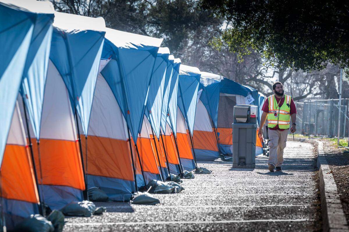 A worker walks near tents at the new Safe Ground homeless site on its opening day in February in Sacramento’s Miller Regional Park on the Sacramento River. Unhoused individuals will have access to bathrooms, showers, drinking water, trash pickup, as well as medical, mental health and rehousing services. The area will be fenced with around-the-clock staffing.