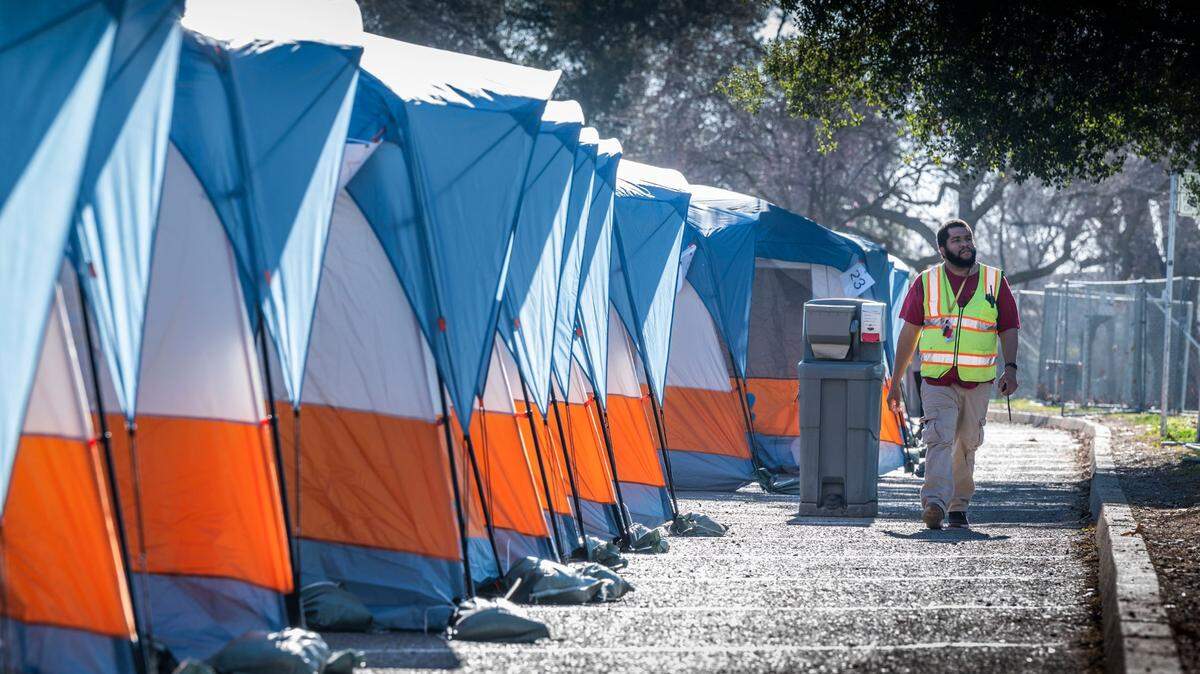 A worker walks near tents at the new Safe Ground homeless site on its opening day, Monday, Feb. 7, 2022, in Sacramento’s Miller Regional Park on the Sacramento River. Roughly 60 tents are set up along Marina View Drive. Unhoused individuals will have access to bathrooms, showers, drinking water, trash pickup, as well as medical, mental health and rehousing services. The area will be fenced with around-the-clock staffing.