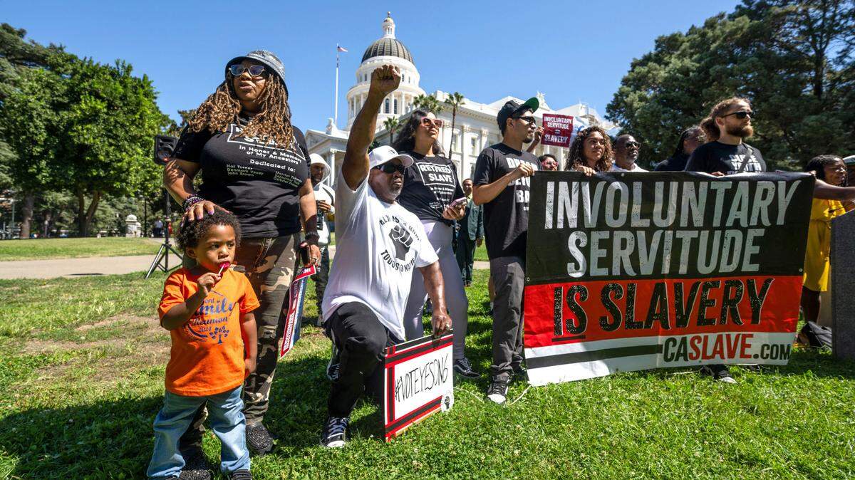 Beatrice X Johnson, with her 2-year old grandson, Akua, and Curtis Howard, raising his fist, join a campaign kickoff rally for Proposition 6 at the state Capitol on Tuesday, Sept. 3, 2024. The measure would change the state Constitution to ban involuntary servitude in California jails and prisons. Currently inmates can be compelled to work and punished with solitary confinement if they refuse. Supporters, many wearing “retired slave” T-shirts held dual events in Sacramento and Los Angeles.