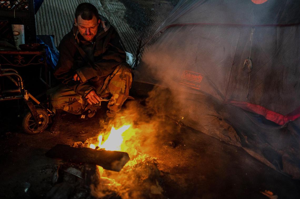 Chris Lewis tries to stay warm with a small fire at a homeless camp on 26th Street under the W-X freeway in Sacramento on Thursday. Karen Hunter died on Tuesday night two tents down from him during a severe winter storm.