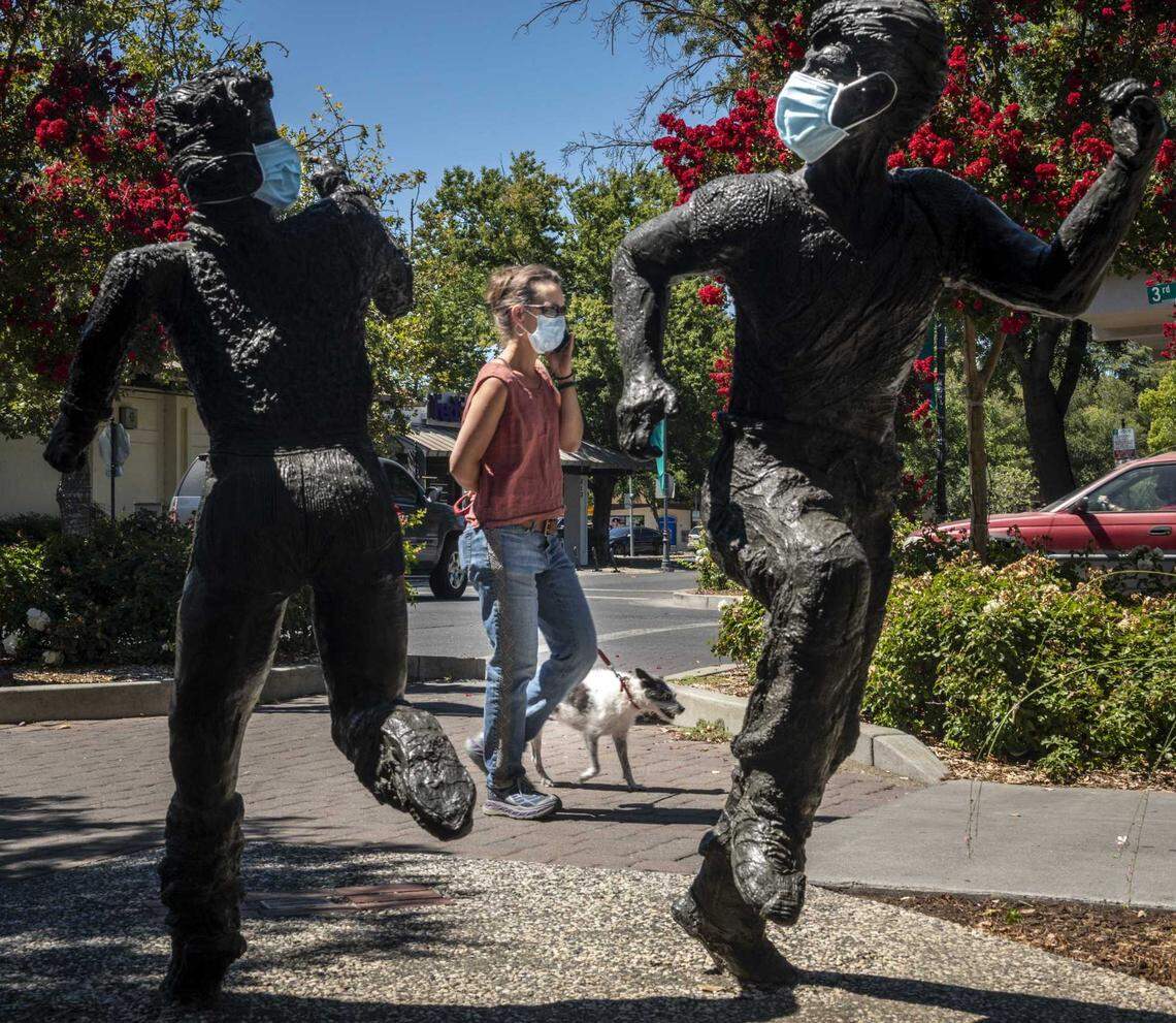 A woman walks with her dog near masked statues of children running on July 22, 2020, in Davis.