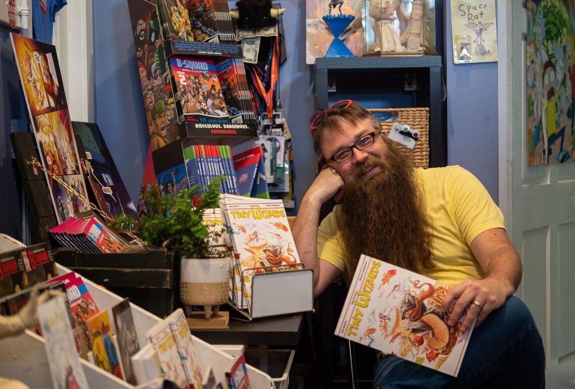 Sacramento comic book writer and cartoonist Eben Burgoon sits by some of his older work while holding his newest comic, “Tiny Wizards,” on Tuesday in his studio at Sierra 2 Center. With assistance of about $8,000 in grant funding in 2020, Burgoon was able to continue paying rent – which was cut in half at the center during some of its closure at the height of the COVID-19 pandemic.