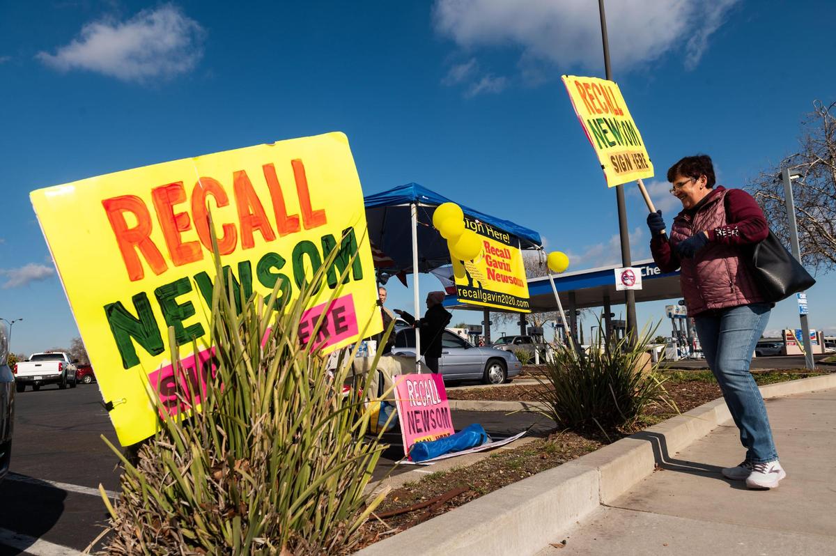A volunteer with the Recall Gavin Newsom campaign, who did not want to be identified, walks back to a signature-collection table set up in the parking lot of Rivergate Shopping Center after holding a sign at the intersection Saturday, Jan. 23, 2021, in Rancho Cordova.