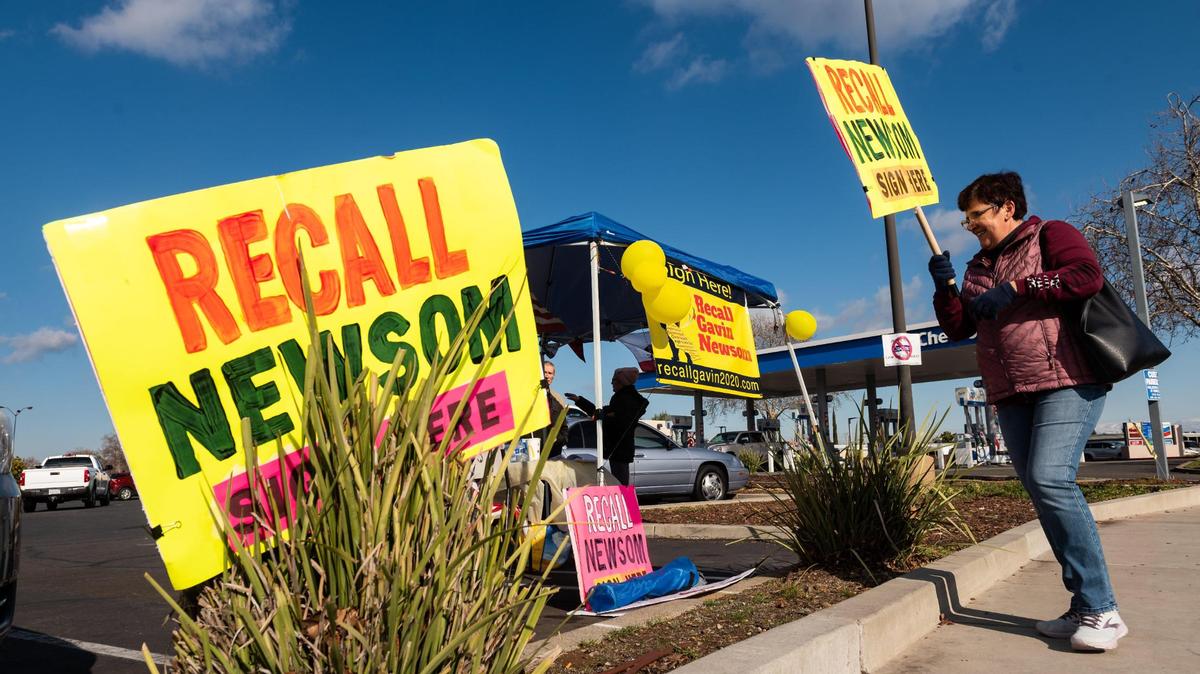 A volunteer with the Recall Gavin Newsom campaign, who did not want to be identified, walks back to a signature-collection table set up in the parking lot of Rivergate Shopping Center after holding a sign at the intersection Saturday, Jan. 23, 2021, in Rancho Cordova.