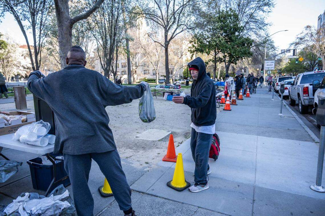 Level Woods, a volunteer of Clothing and Food for Everyone, gives Edward Delgado a bag of food earlier this month, at Cesar Chavez Plaza. The program, founded by Armando Flores, has been assisting homeless and those in need at the park.