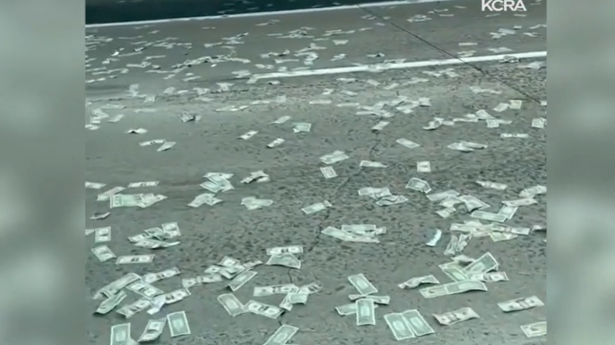 Money is shown scattered across the Interstate 5 in Carlsbad, California, on Nov. 19, 2021, after an armored car’s door opened. Two people were arrested after they were accused of picking money up, officials said.