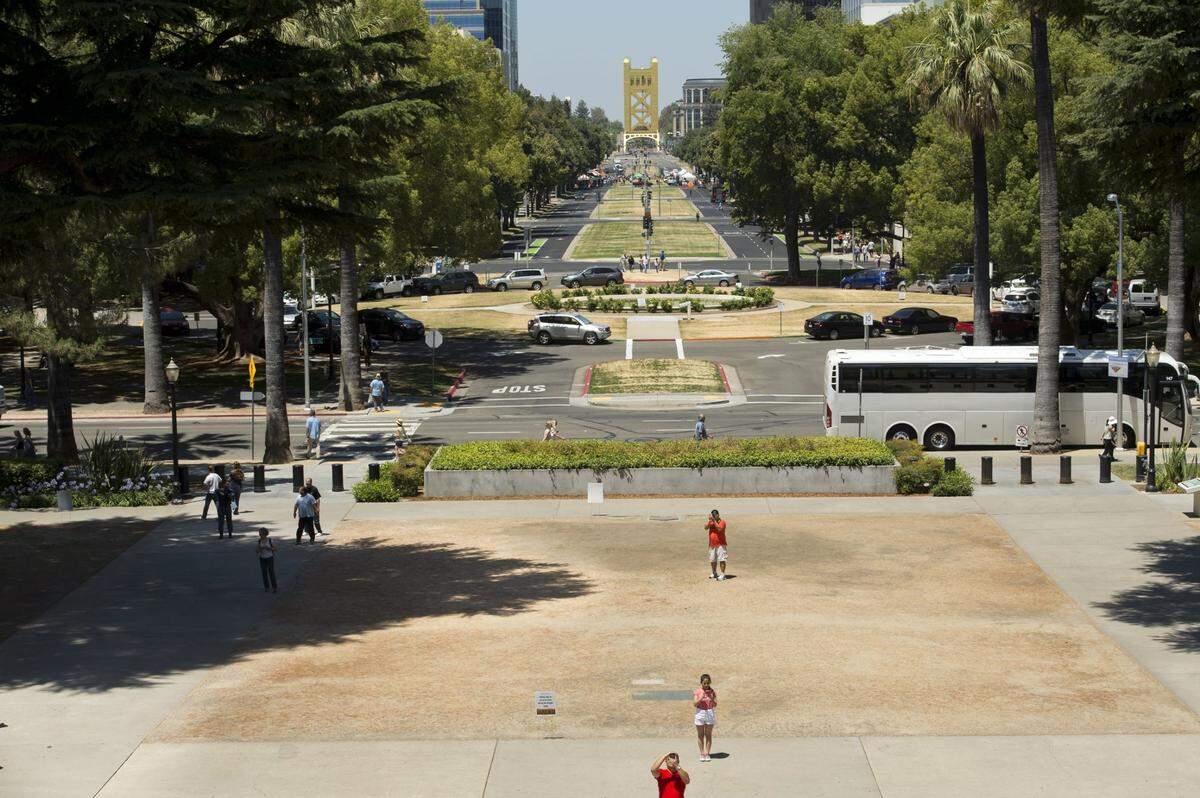 Tourists take photographs of the state Capitol in Sacramento in 2014 on the brown grass of the Capitol grounds. The turf was allowed to die to show California residents the seriousness of the drought and set an example for water use. “It’s California’s front yard,” said Brian Ferguson, a spokesman for the Department of General Services. “We”re trying to set an example in our front yard of what they can do in their front yards.”