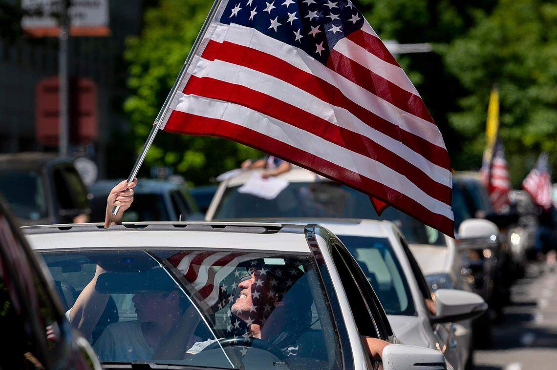Annette Rotd waves the American flag as her husband, Jay, drives down N Street during a demonstration at the Capitol in Sacramento on Friday, May 1, 2020, against Gov. Gavin’s Newsom’s stay-at-home order.