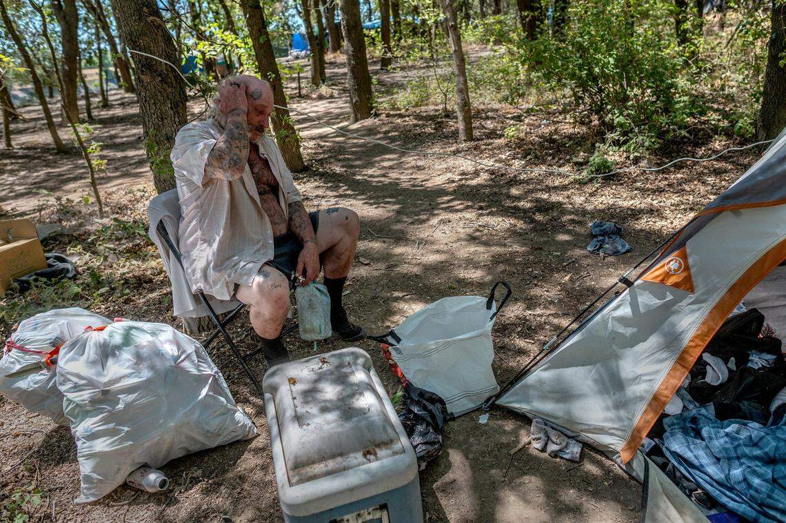 Robert Burton, 58, who goes by “Clownboy,” clutches a bag of medicine while sitting outside his tent on July 6. He has stage four liver cancer and said he wanted to die at the camp where he lived for 18 years. He’s since left and gone into hospice care.