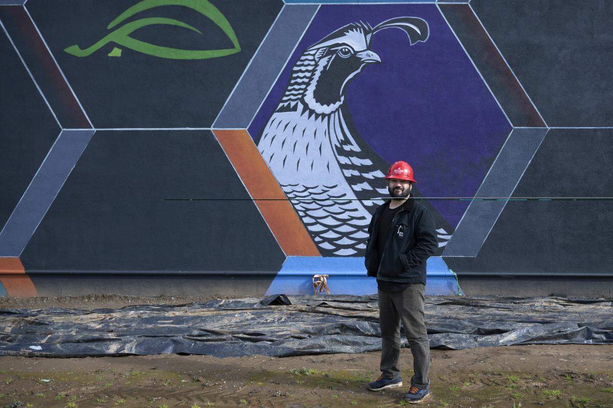 Artist Raphael Delgado stands in front of a mural he is working on at the R21 housing development in Sacramento on Thursday.