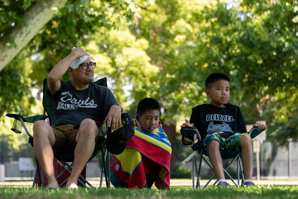 Van Tran wipes the sweat from his head while sitting in the shade on a 103 degree day in Sacramento on Friday, June 30, 2023, with his sons Levi, 11, and Gavin, 8, after a swim at Clunie Pool to cool off.
